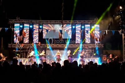 Salle avec éclairage de scène coloré, piste de danse illuminée, tables sur les côtés et matériel audio en arrière-plan.