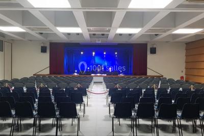 Salle avec éclairage de scène coloré, piste de danse illuminée, tables sur les côtés et matériel audio en arrière-plan.