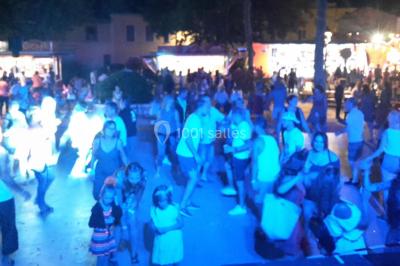 Salle avec éclairage de scène coloré, piste de danse illuminée, tables sur les côtés et matériel audio en arrière-plan.