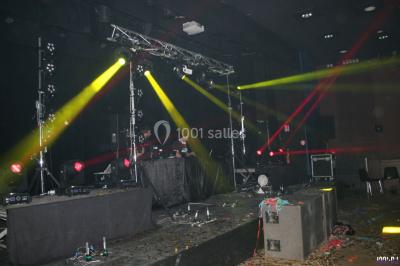 Salle avec éclairage de scène coloré, piste de danse illuminée, tables sur les côtés et matériel audio en arrière-plan.