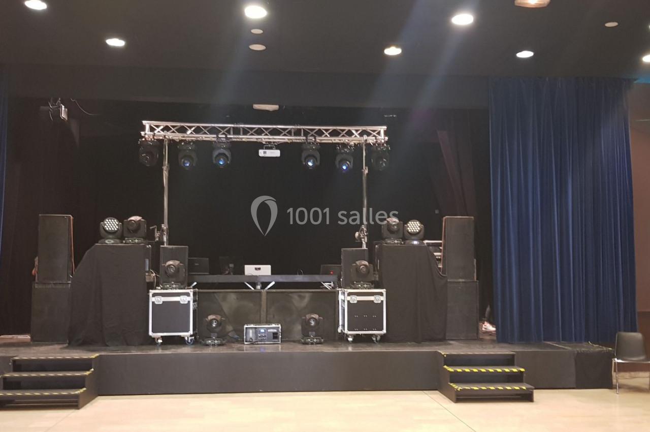 Scène équipée de matériel de sonorisation et d'éclairage, entourée de rideaux bleus dans une salle de spectacle.