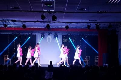 Salle avec éclairage de scène coloré, piste de danse illuminée, tables sur les côtés et matériel audio en arrière-plan.