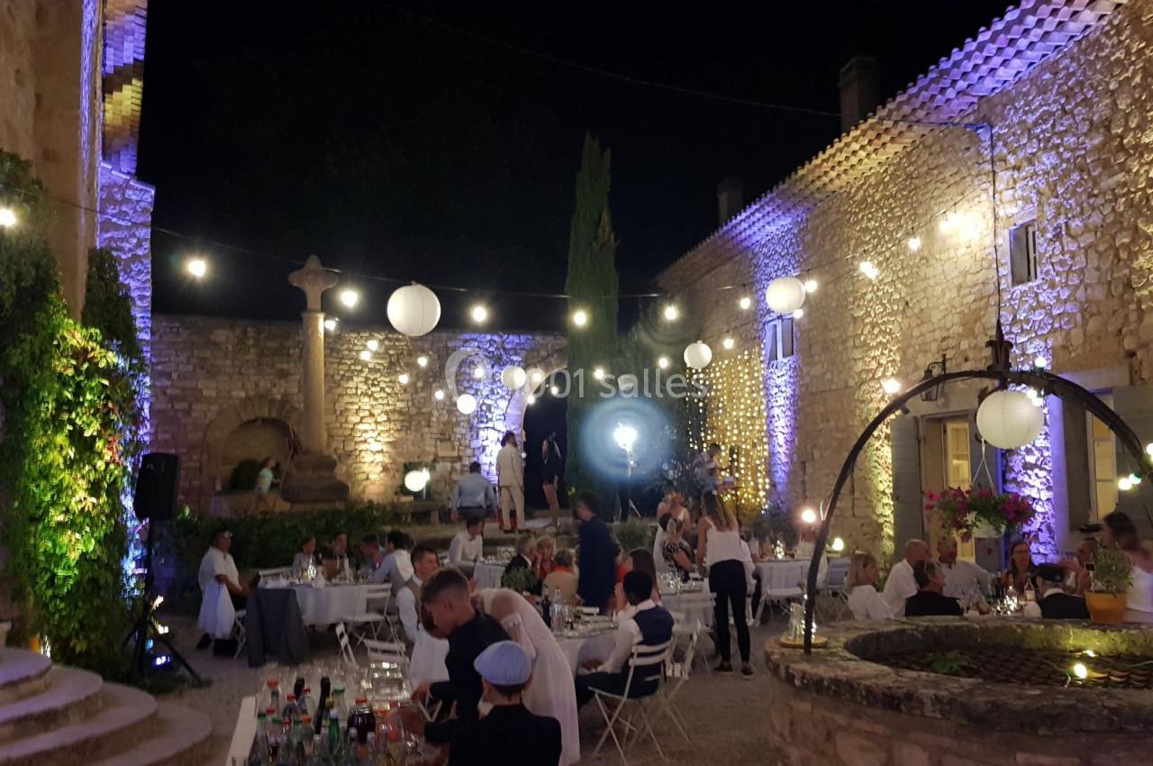 Cour extérieure éclairée la nuit, décorée de guirlandes lumineuses, avec des tables dressées et des invités réunis.