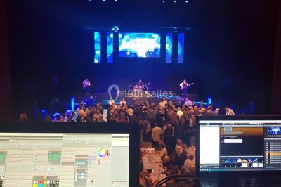 Salle avec éclairage de scène coloré, piste de danse illuminée, tables sur les côtés et matériel audio en arrière-plan.