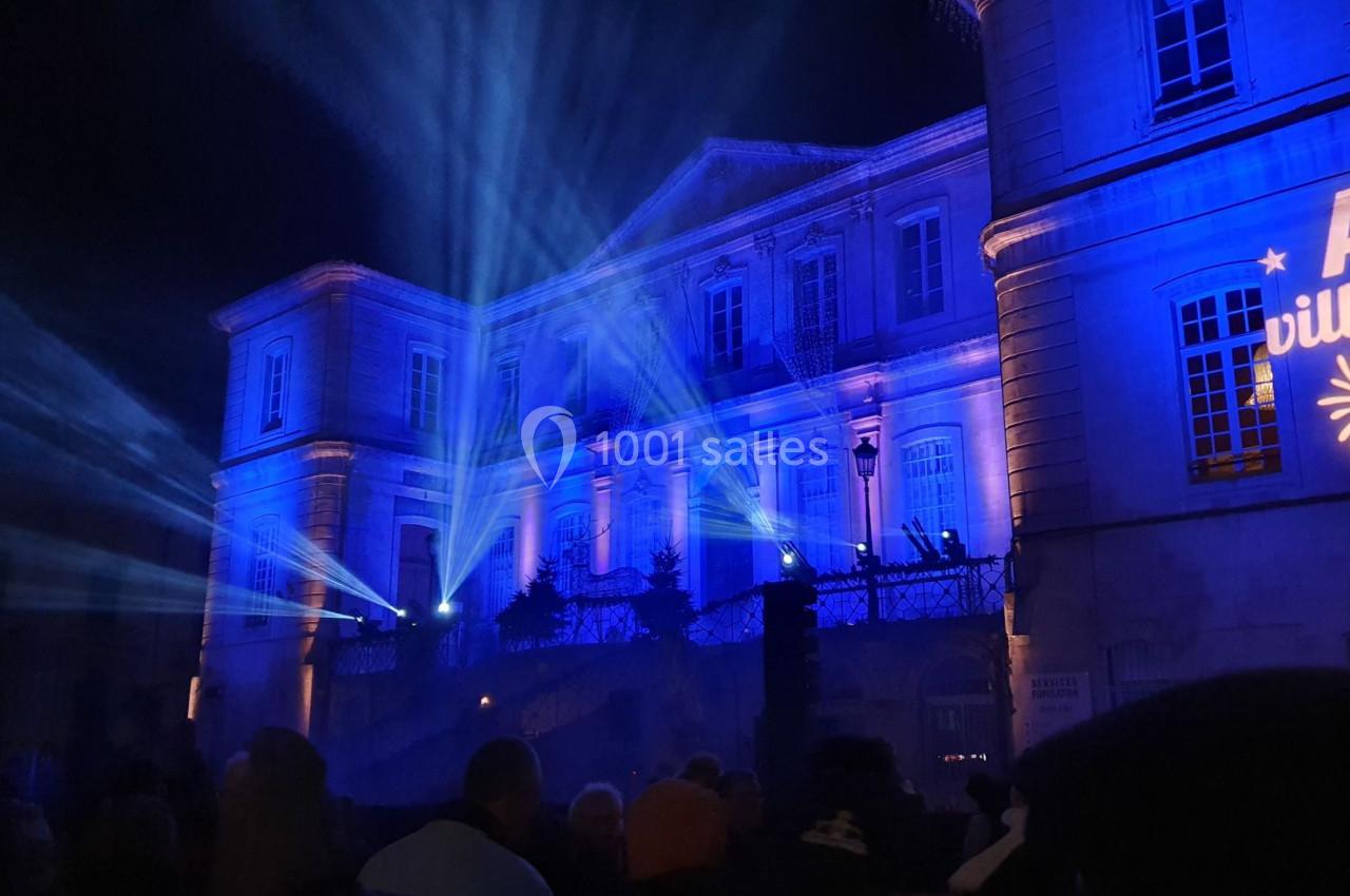 Façade d'un bâtiment illuminée en bleu avec des projections lumineuses et une foule rassemblée devant.