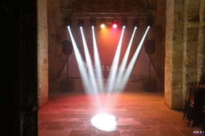 Salle avec éclairage de scène coloré, piste de danse illuminée, tables sur les côtés et matériel audio en arrière-plan.
