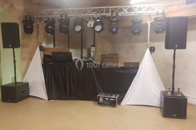 Salle avec éclairage de scène coloré, piste de danse illuminée, tables sur les côtés et matériel audio en arrière-plan.