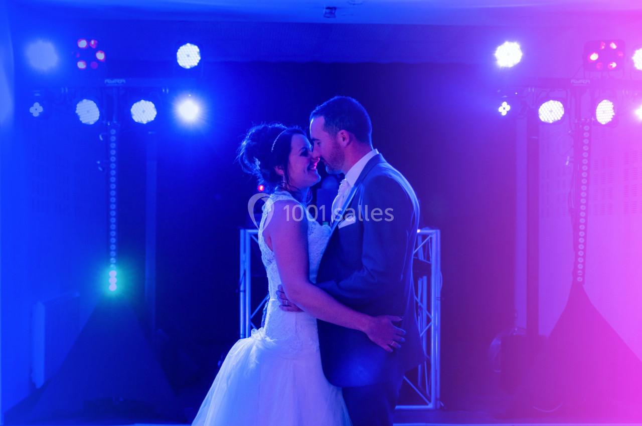 Un couple en tenue de mariage danse sous des lumières colorées dans une ambiance festive.