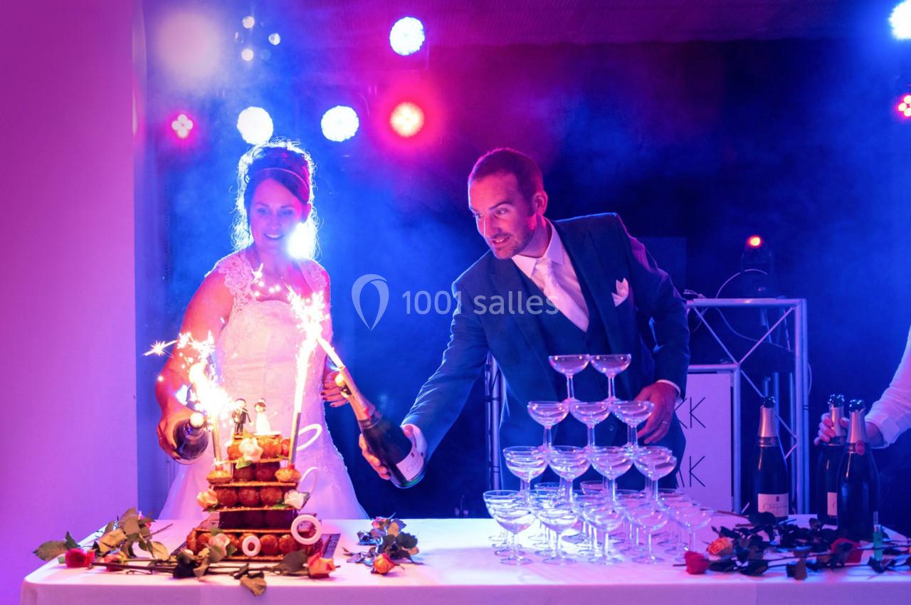 Un couple en tenue de mariage verse du champagne sur une pyramide de verres illuminée par des étincelles.