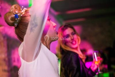 Deux femmes dansent et discutent dans une ambiance festive avec des lumières colorées.