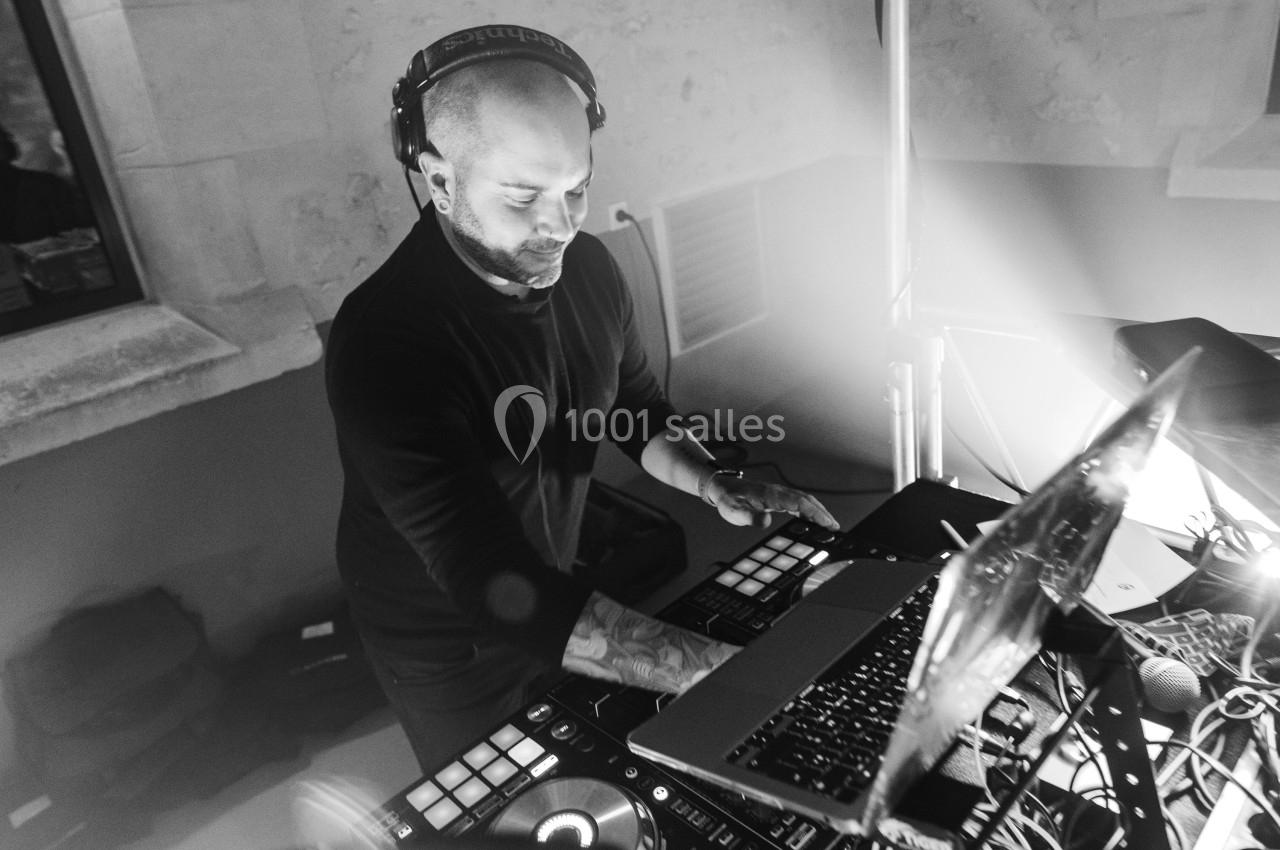 Un DJ mixant de la musique sur une table de mixage entourée d'équipements électroniques dans une ambiance lumineuse.