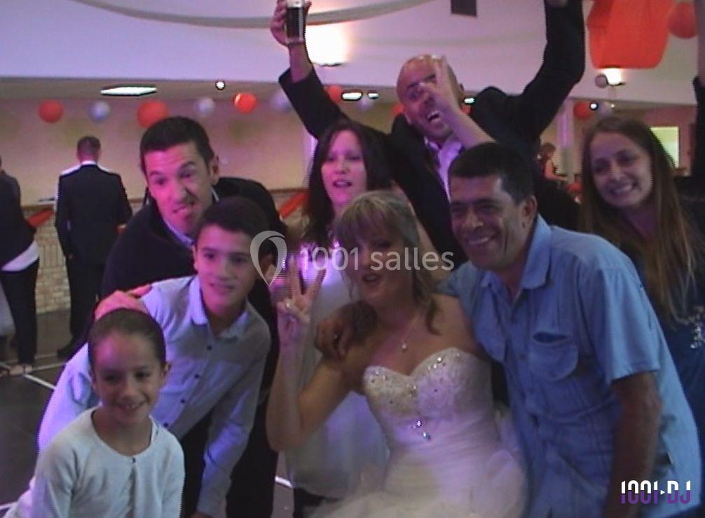 Un groupe de personnes souriantes pose lors d'une fête, avec une mariée en robe blanche au centre.