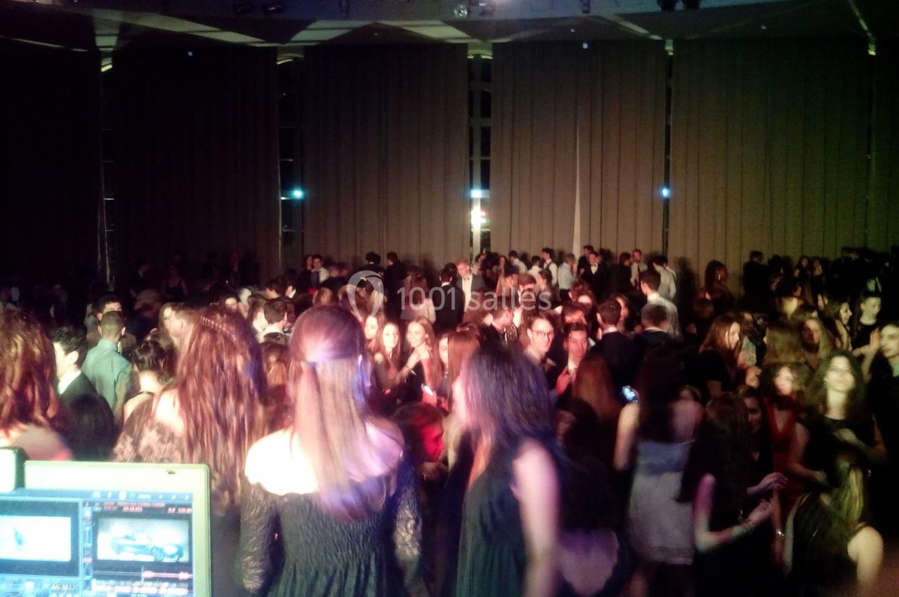 Des personnes dansent dans une salle sombre avec des rideaux fermés, vue depuis une table de mixage.