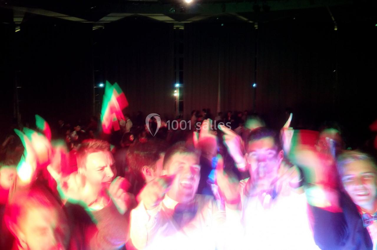 Groupe de personnes dansant dans une ambiance festive avec des lumières colorées et un drapeau visible en arrière-plan.