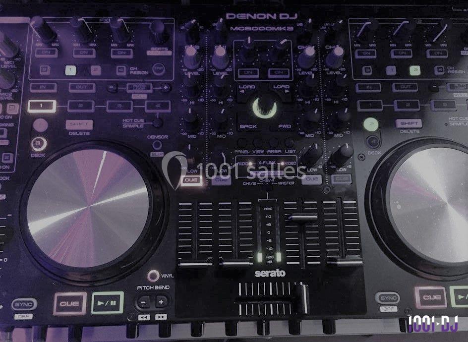 Table de mixage Denon DJ avec boutons, curseurs et deux plateaux rotatifs éclairés par des lumières violettes.