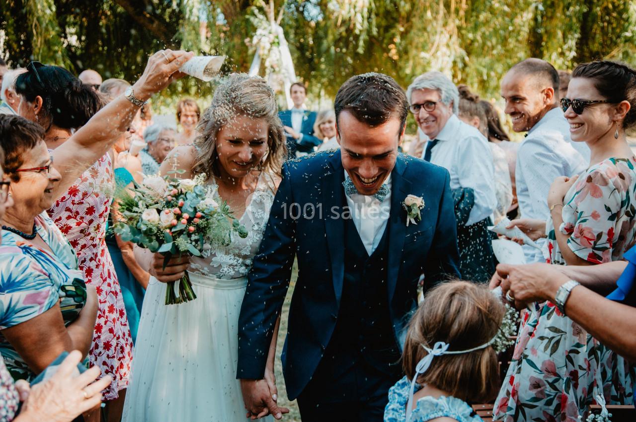 Un couple souriant sort sous une pluie de confettis entouré d'invités lors d'une cérémonie en extérieur.
