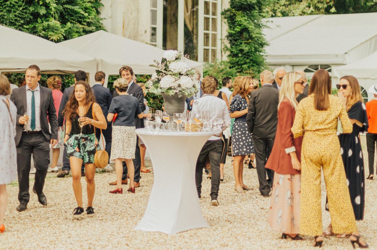 Groupe de personnes discutant et partageant des boissons lors d'un événement en extérieur avec des tentes blanches.