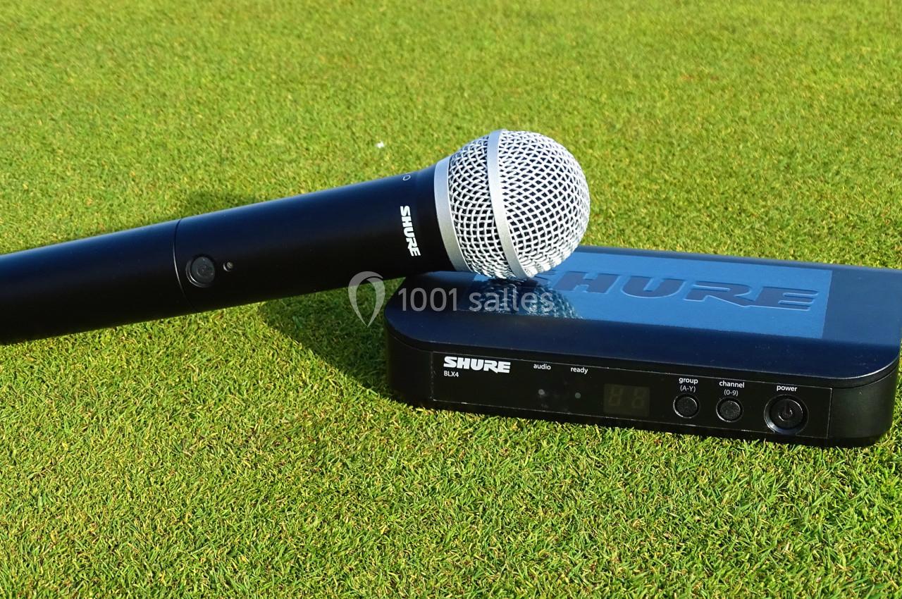 Microphone sans fil noir et récepteur posés sur une pelouse verte.