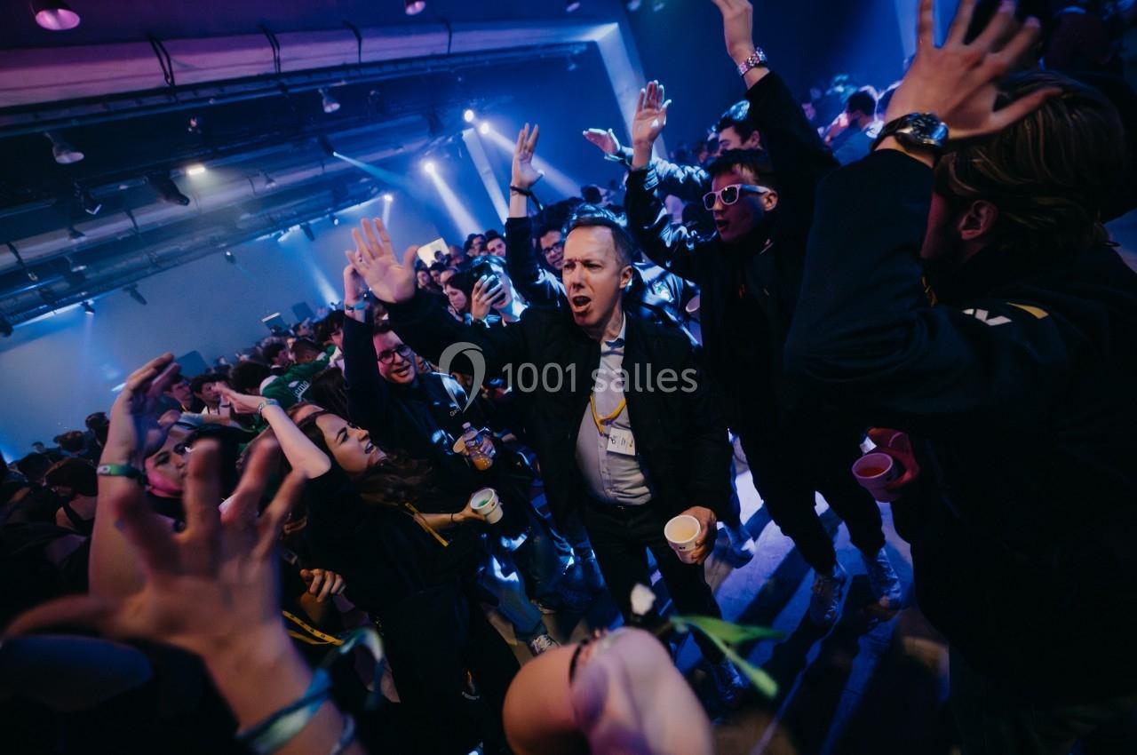 Des personnes dansent et lèvent les bras dans une ambiance festive, éclairée par des lumières colorées.