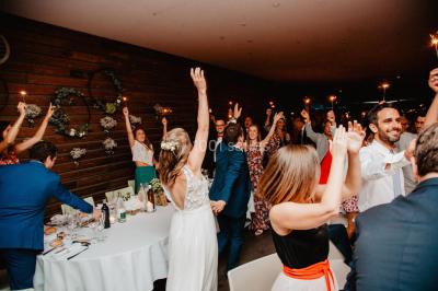 Des invités dansent et célèbrent sous une tente décorée, autour d'une mariée et d'un homme en costume.