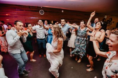 Des invités dansent et célèbrent sous une tente décorée, autour d'une mariée et d'un homme en costume.