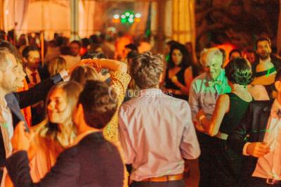 Des invités dansent et célèbrent sous une tente décorée, autour d'une mariée et d'un homme en costume.