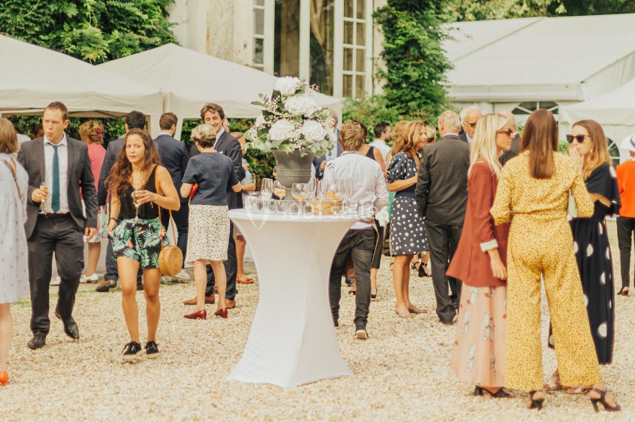 Groupe de personnes discutant et se tenant debout dans un jardin, près de tables hautes décorées de fleurs blanches.