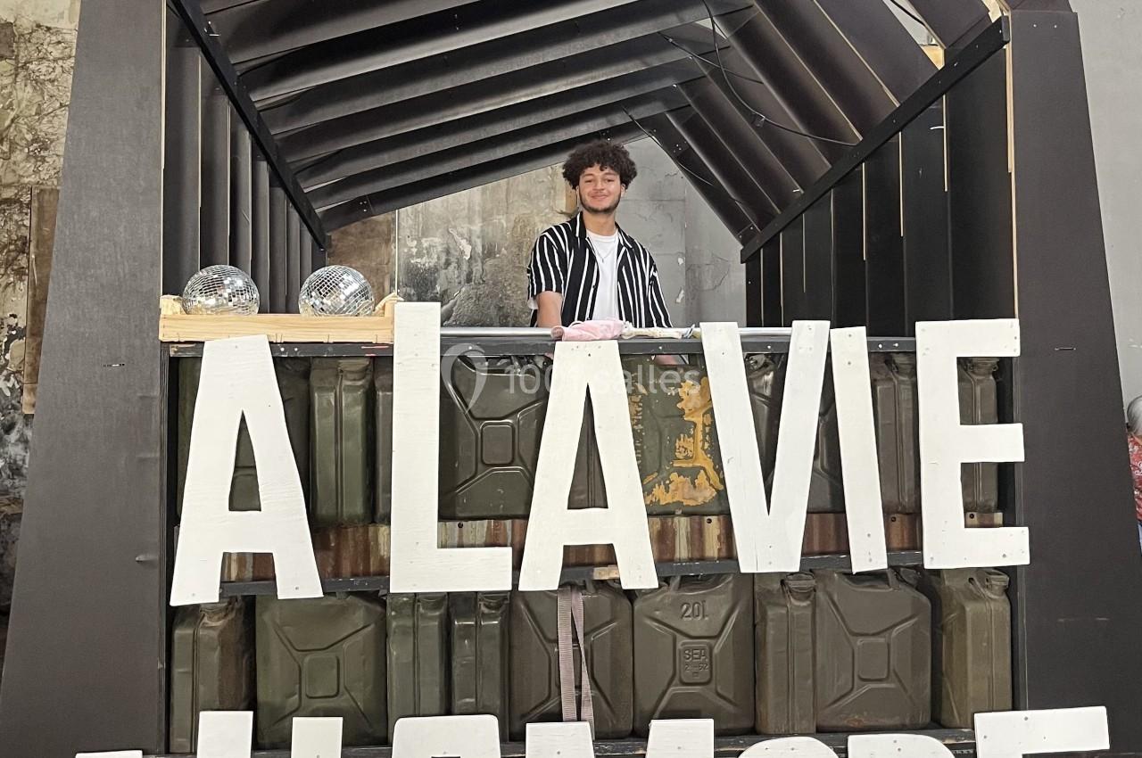 Stand décoratif avec une personne souriante derrière un comptoir, affichant les mots ’À la vie, à l'amore’.