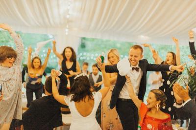 Des invités dansent et célèbrent sous une tente décorée, autour d'une mariée et d'un homme en costume.