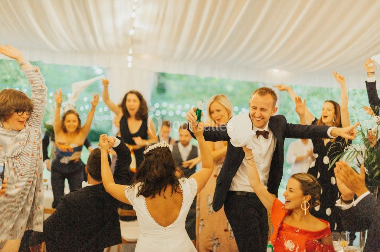 Des invités dansent et célèbrent sous une tente décorée, autour d'une mariée et d'un homme en costume.