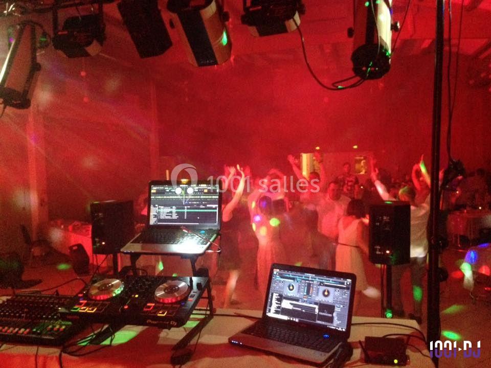 Vue depuis la table de mixage d'un DJ, avec des invités dansant sous des lumières colorées dans une salle.