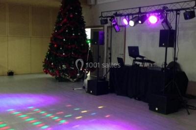 Salle décorée avec un sapin de Noël, éclairages colorés au sol et matériel de DJ installé sur une estrade.