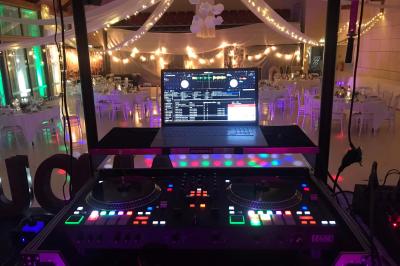 Salle décorée avec un sapin de Noël, éclairages colorés au sol et matériel de DJ installé sur une estrade.