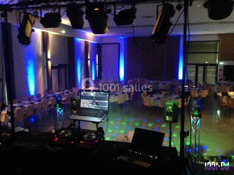 Salle de réception éclairée avec des lumières colorées, vue depuis une table de mixage avec ordinateur et équipements DJ.