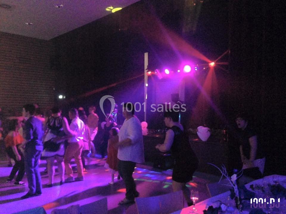 Des personnes dansent sur une piste éclairée par des lumières colorées lors d'une fête en intérieur.