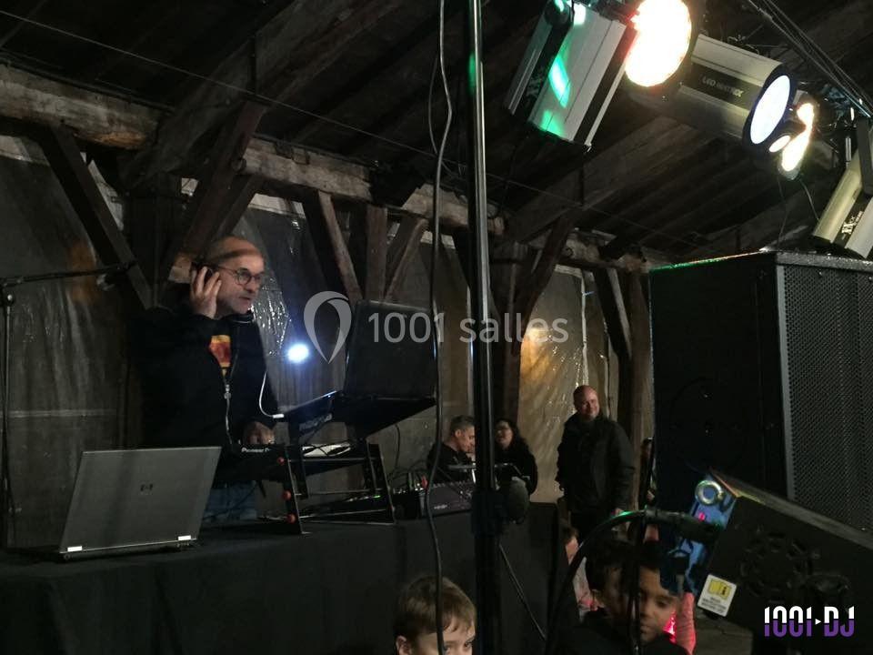 Un DJ mixe sur une scène sous une structure en bois, avec des lumières colorées et un public en arrière-plan.