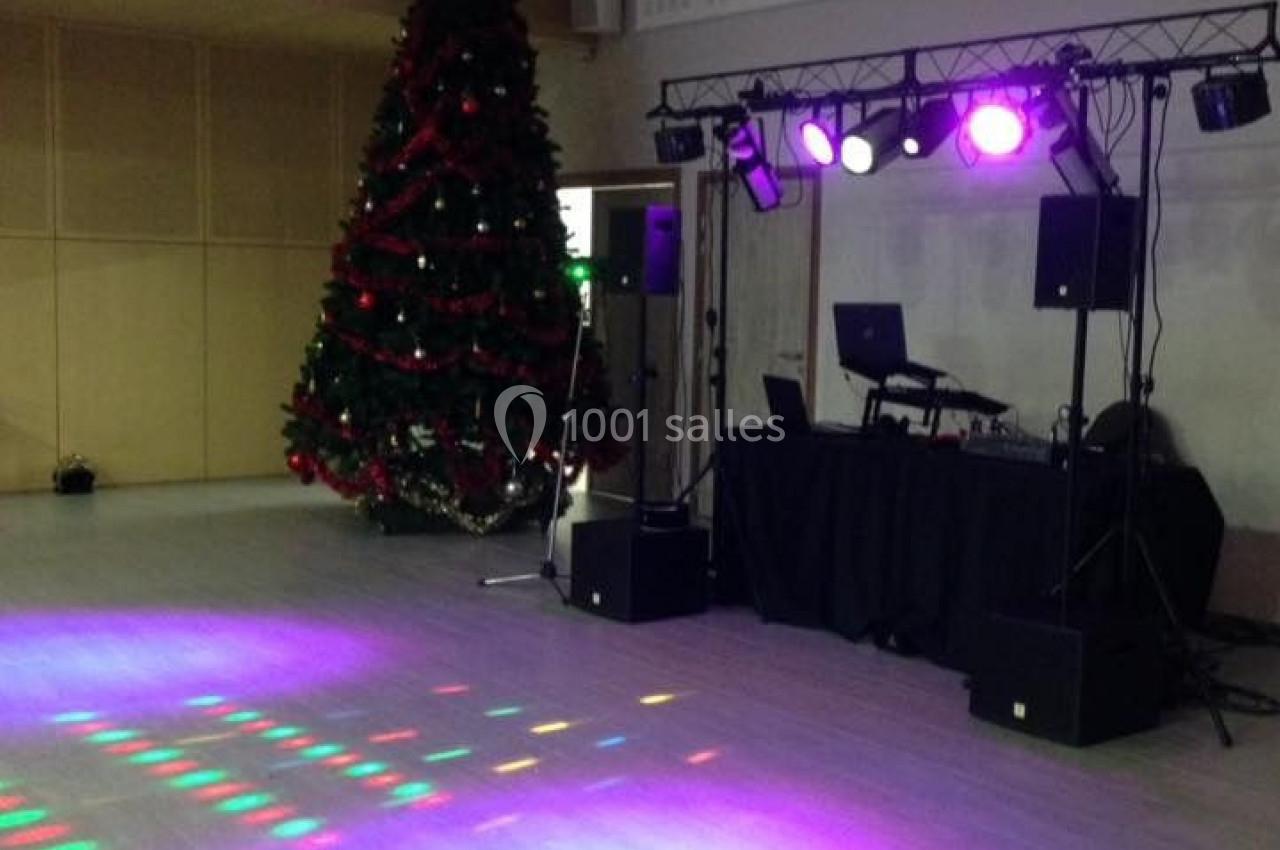 Salle décorée avec un sapin de Noël, éclairages colorés au sol et matériel de DJ installé sur une estrade.