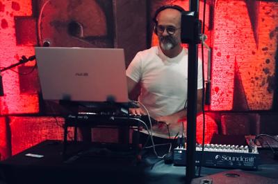 Un DJ portant un casque mixe de la musique sur une table de mixage dans un environnement extérieur couvert.