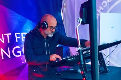 Un DJ portant un casque mixe de la musique sur une table de mixage dans un environnement extérieur couvert.