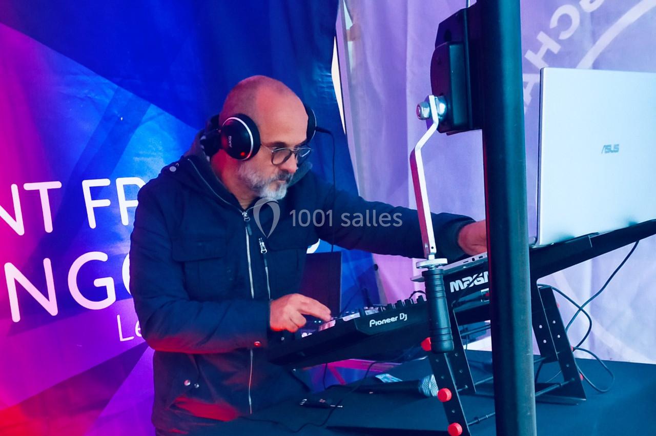 Un DJ portant un casque mixe de la musique sur une table de mixage dans un environnement extérieur couvert.