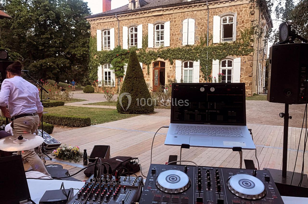 Matériel de DJ installé en extérieur devant une grande maison en pierre avec jardin et allée pavée.