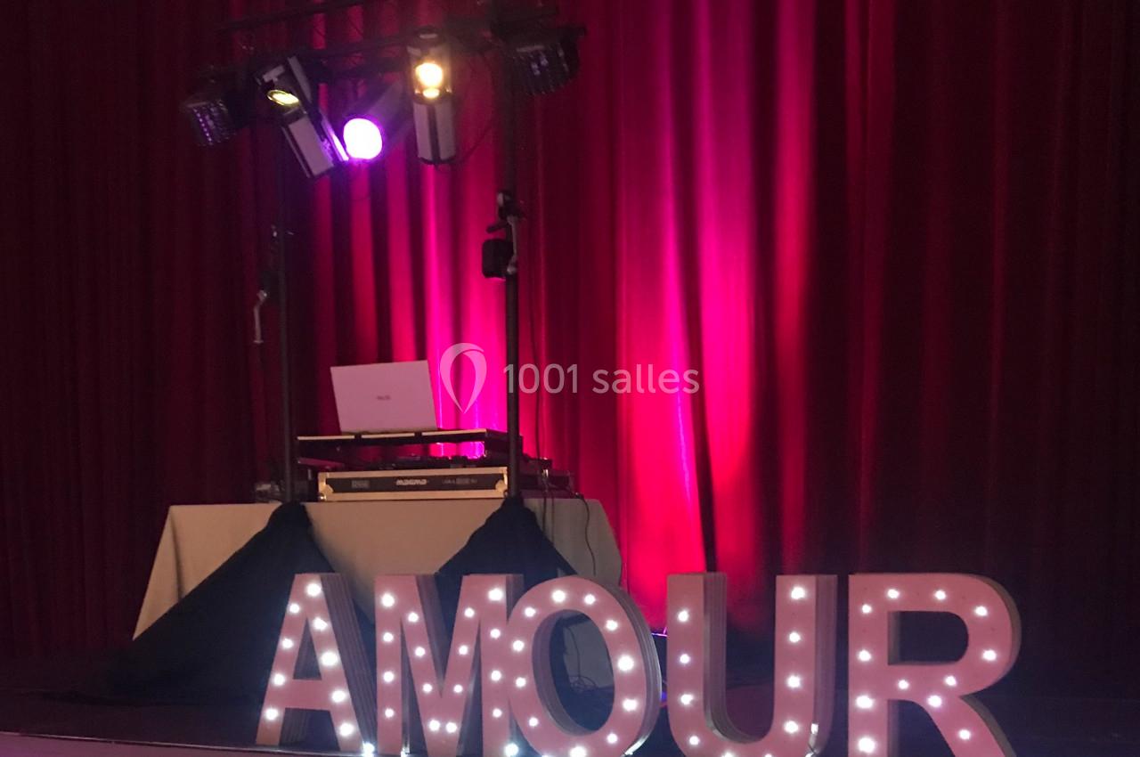 Installation de DJ avec éclairage coloré devant des rideaux rouges et lettres lumineuses formant le mot ’AMOUR’.