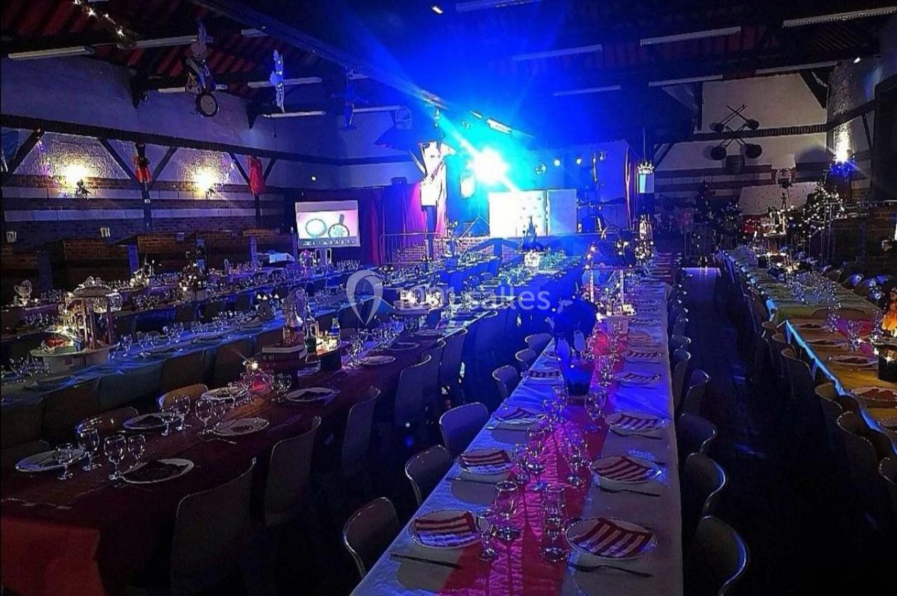 Salle de réception décorée avec des tables dressées pour un événement, éclairée par des lumières colorées.