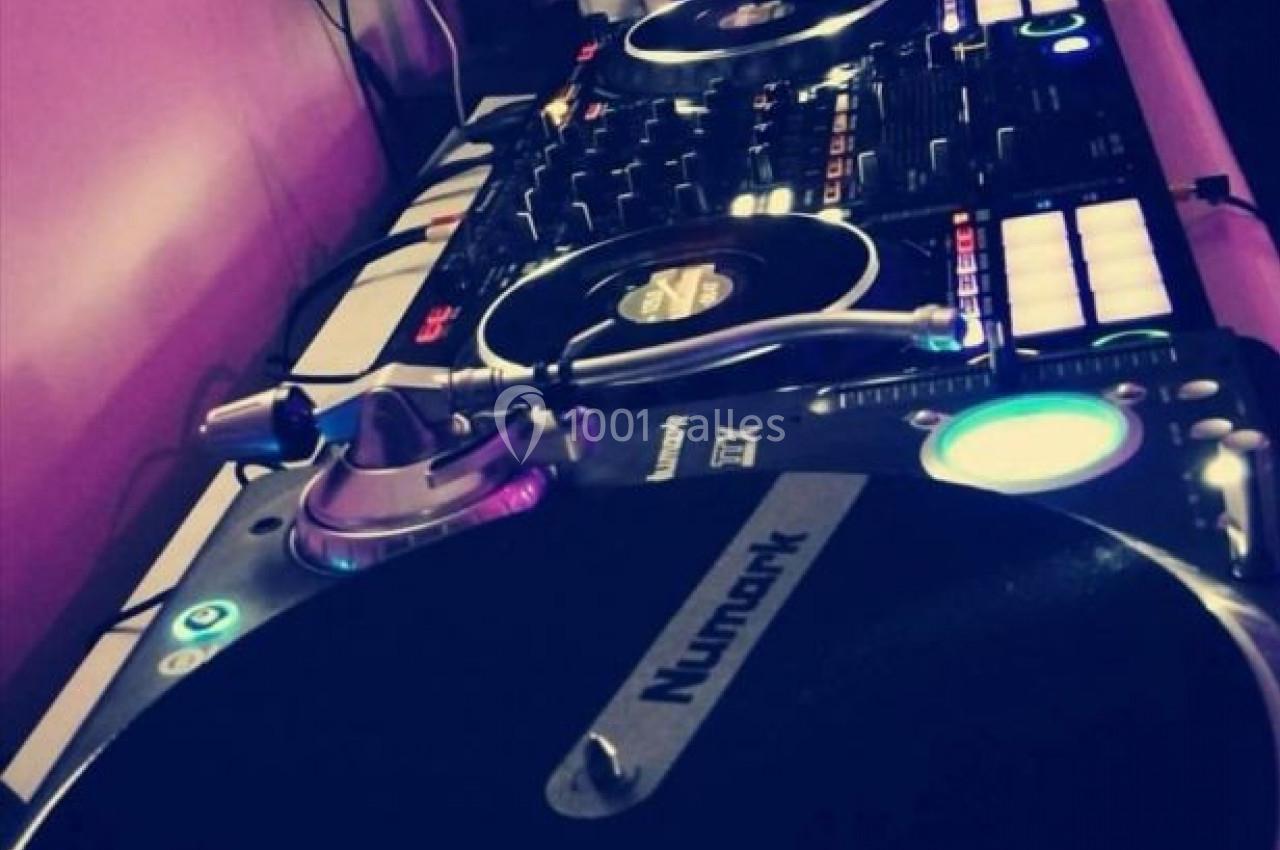 Platines de DJ avec une table de mixage et un ordinateur affichant un logiciel de musique dans un environnement sombre.