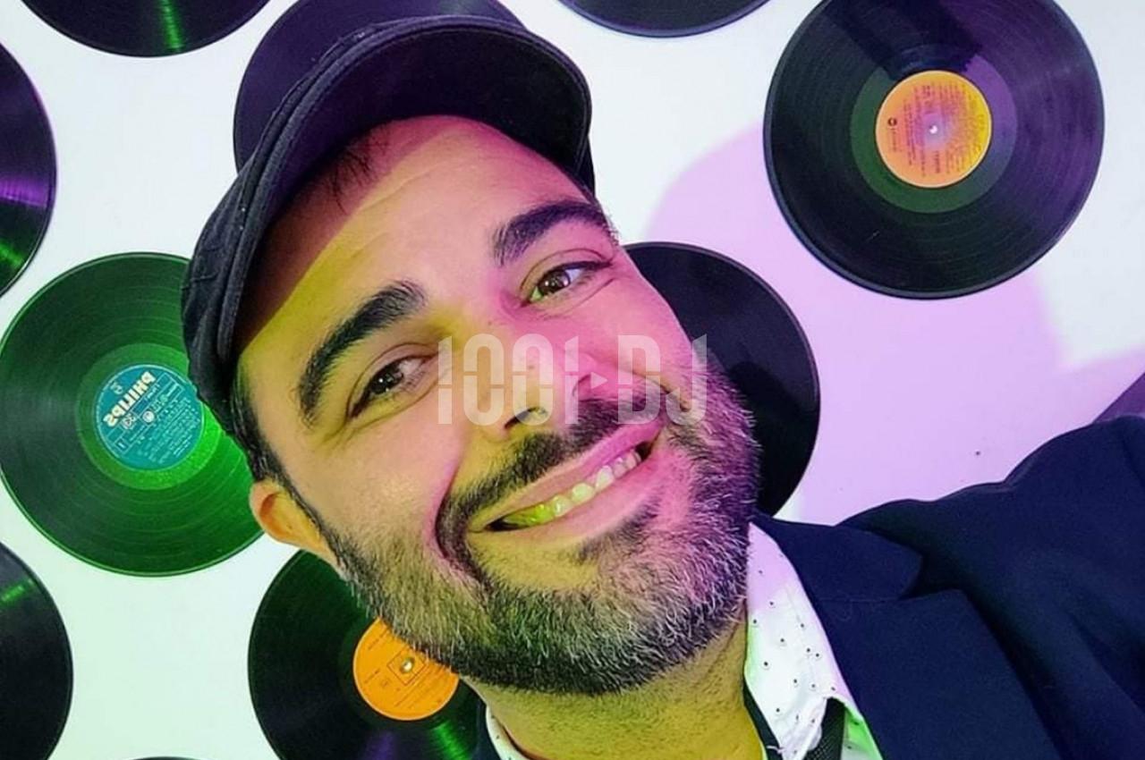 Homme souriant portant une casquette devant un mur décoré de disques vinyles colorés.