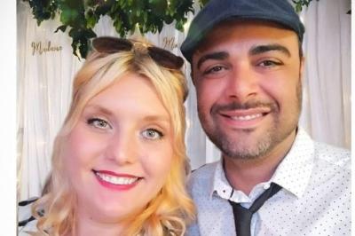 Un homme et une femme sourient devant un fond décoré de feuillage et de rideaux blancs.