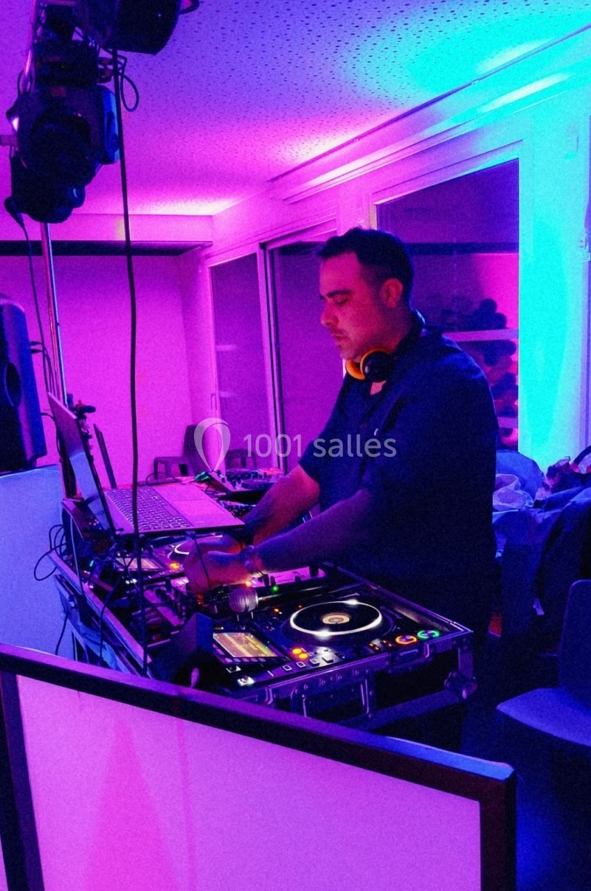 Un DJ mixant de la musique sur une console dans une pièce éclairée par des lumières colorées.