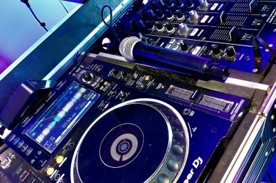 Un DJ en chemise blanche utilise une table de mixage avec des écrans d'ordinateur en arrière-plan.