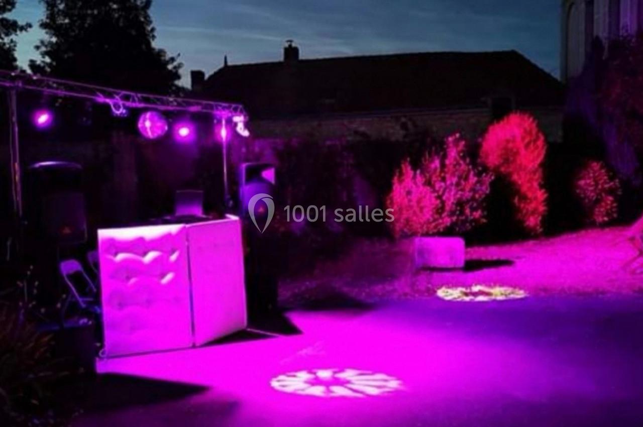Installation de DJ en extérieur avec éclairage violet et projecteurs lumineux, dans un jardin au crépuscule.