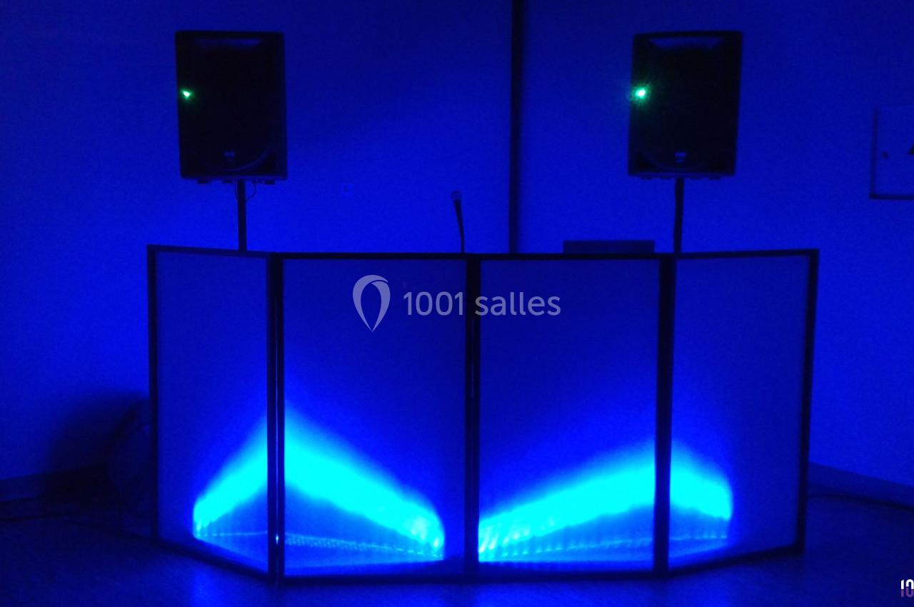 Console de DJ éclairée par des lumières bleues, entourée de deux enceintes sur pieds dans une pièce sombre.